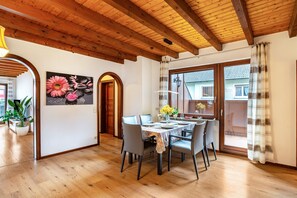 Zona pranzo con soffitto in legno, tavolo apparecchiato per quattro e una grande finestra con vista su una casa.