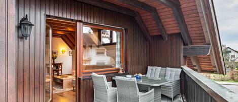 An outdoor patio with wicker furniture, a wooden deck, and a glass door leading to an interior space.