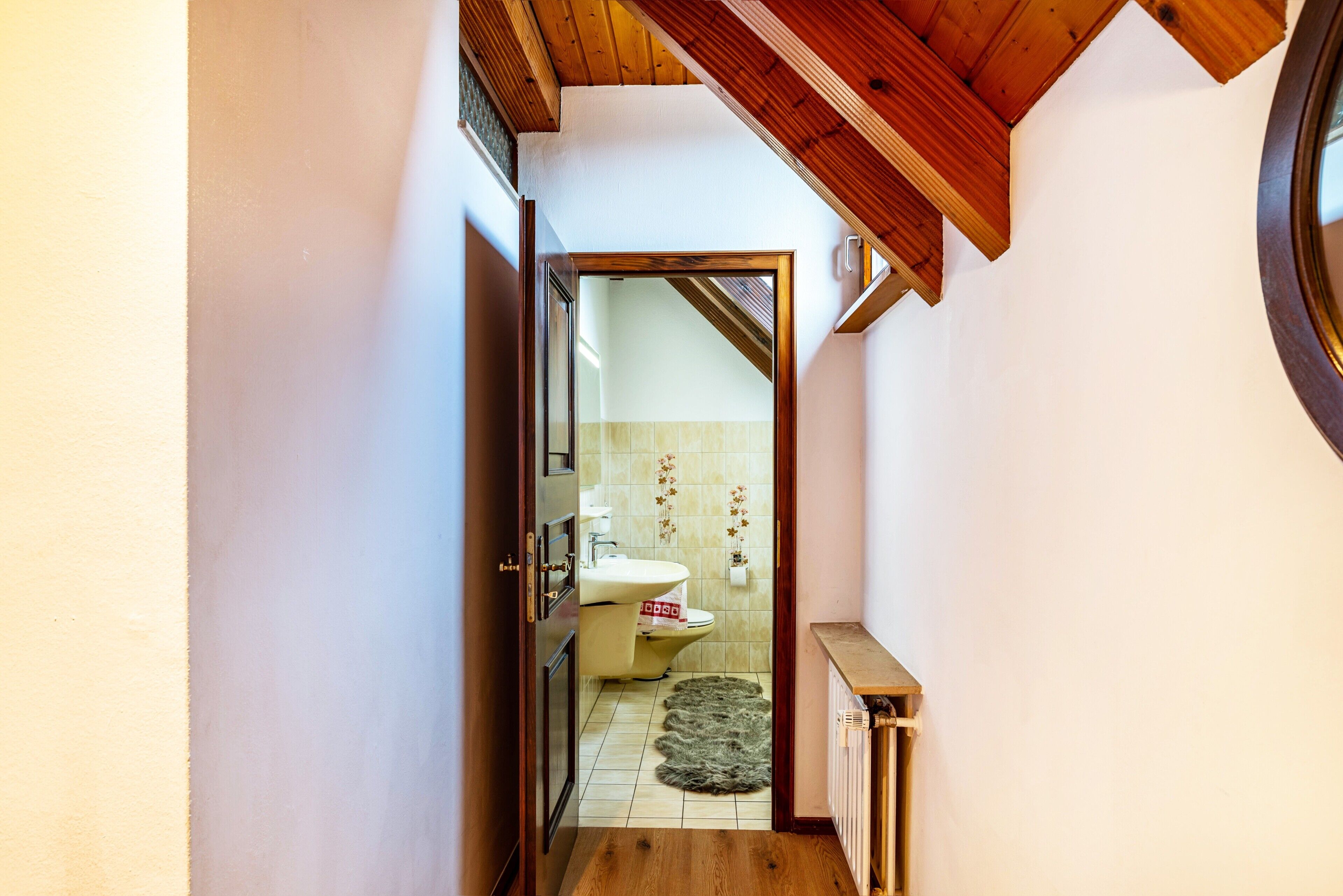 Un pasillo estrecho con techo de madera, una puerta que da al baño y un radiador en el suelo.