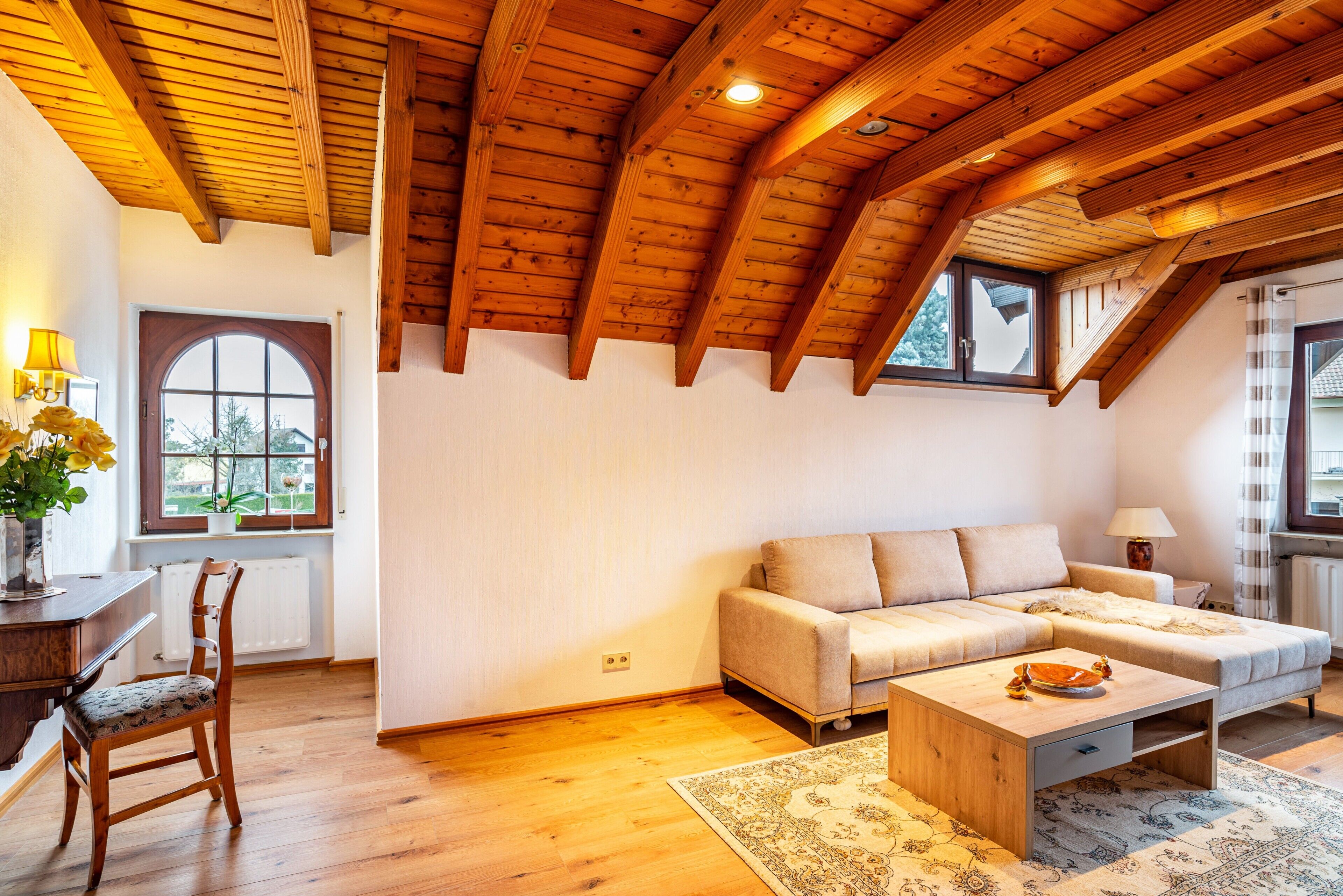 Un loft espacioso con un alto techo de madera, un sofá, una mesa de comedor y vistas a través de un amplio ventanal.