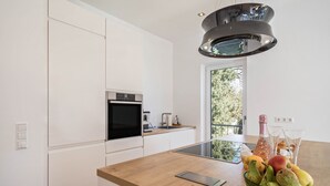 Eine moderne Küche mit Einbauofen, einer Kochinsel mit Glasplatte und einer Pendelleuchte.