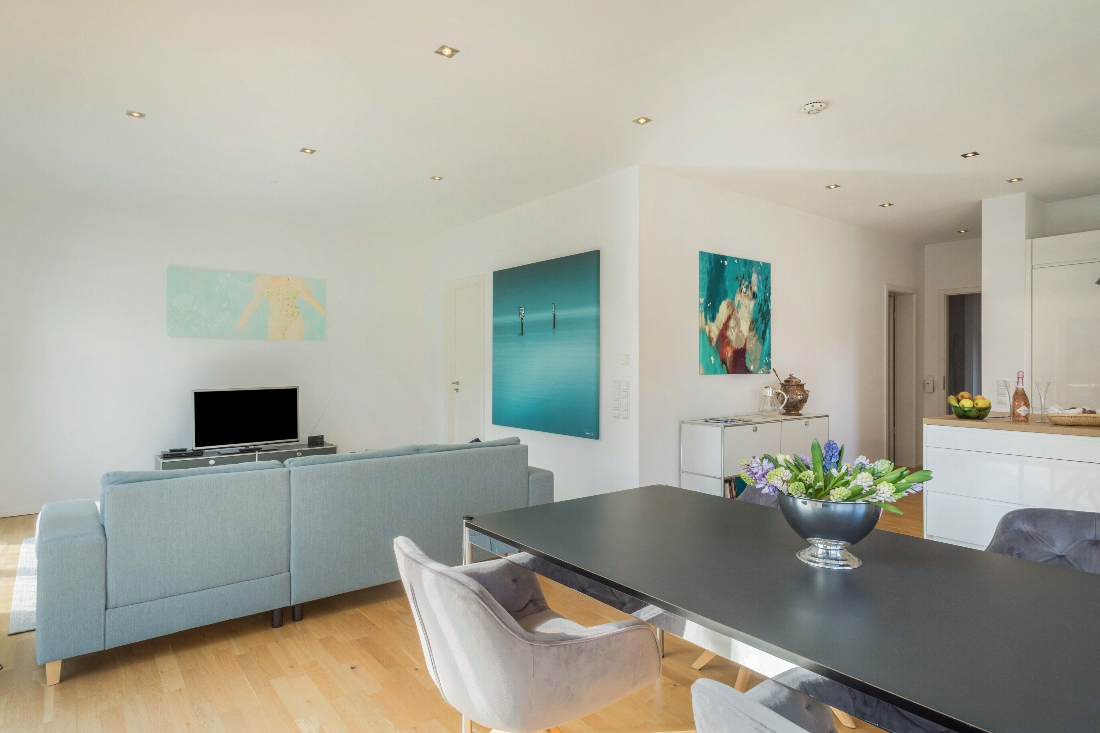 A modern living room with a sofa, a dining table, and artwork on the walls.