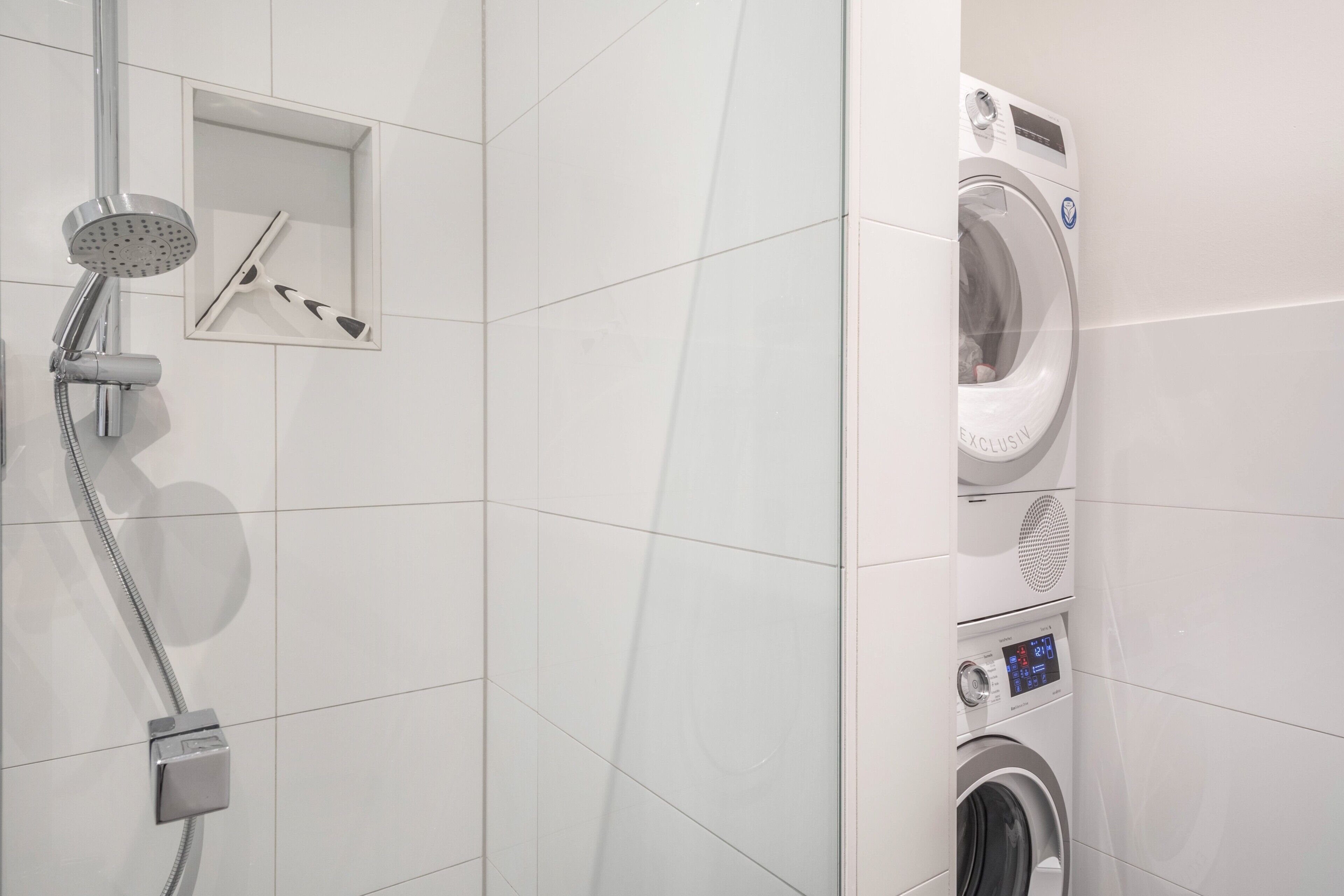 Un baño moderno con ducha integrada, lavadora empotrada y un estante pequeño.