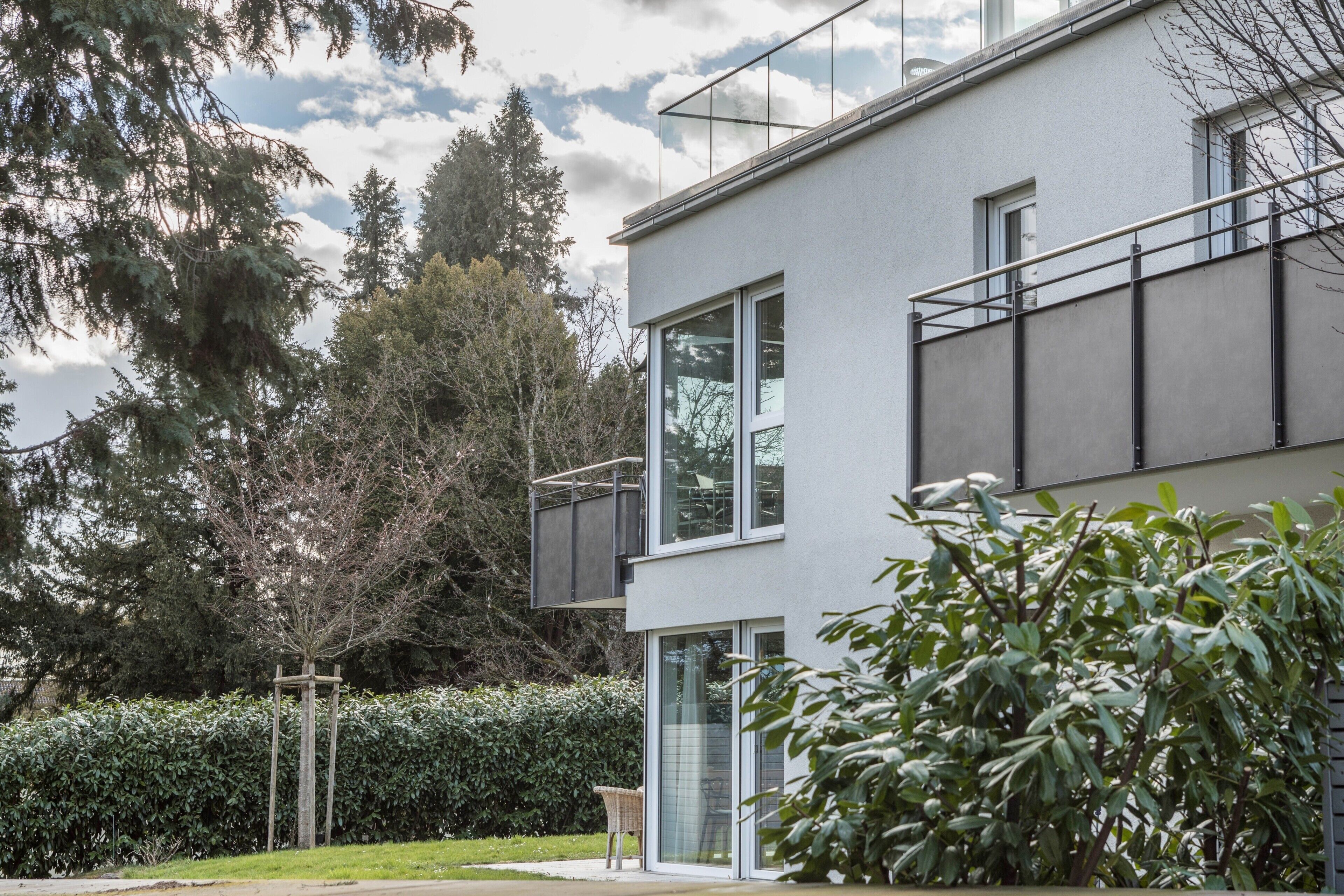 Een modern, twee verdiepingen hoog gebouw met grote ramen, een balkon en een verzorgde tuin.