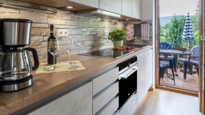 Une cuisine moderne avec un mur recouvert de pierres, des appareils en acier inoxydable et une vue sur un patio extérieur agrémenté de chaises et d’une table.