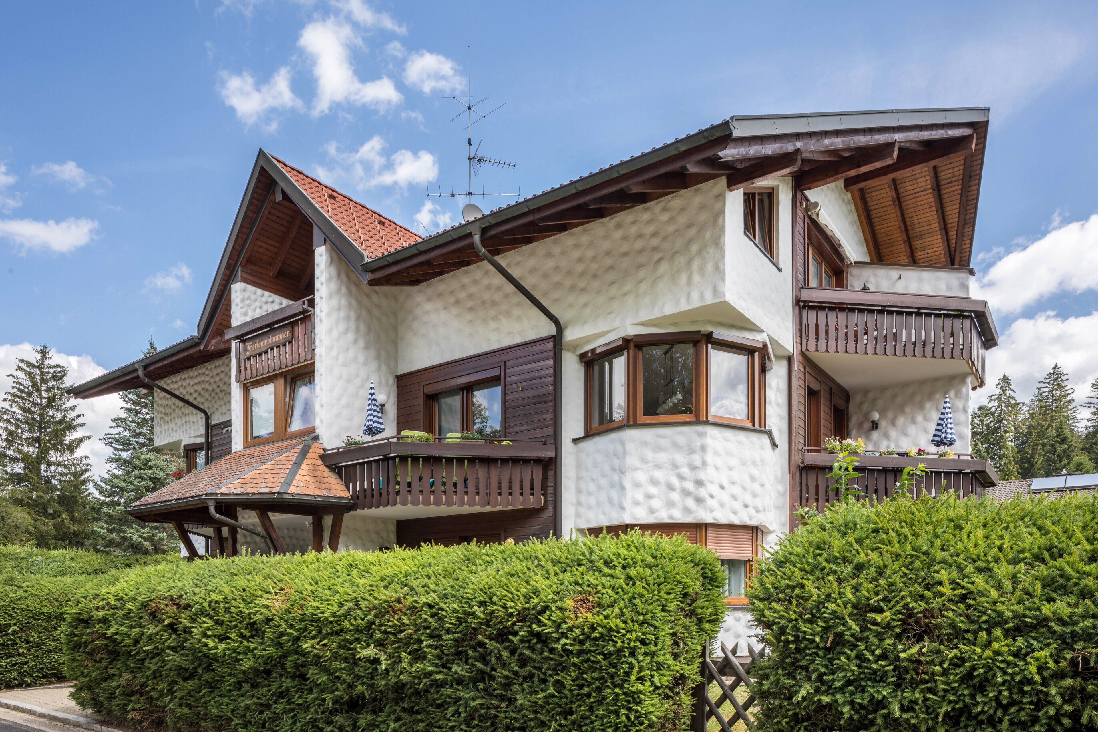 Ein zweigeschossiges Haus mit einem Balkon, einer Satellitenschüssel und einem gepflegten Heckenstreifen.