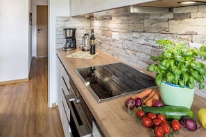 Une cuisine avec un dosseret en pierre, une cuisinière encastrée, une machine à café et des légumes frais sur le plan de travail.
