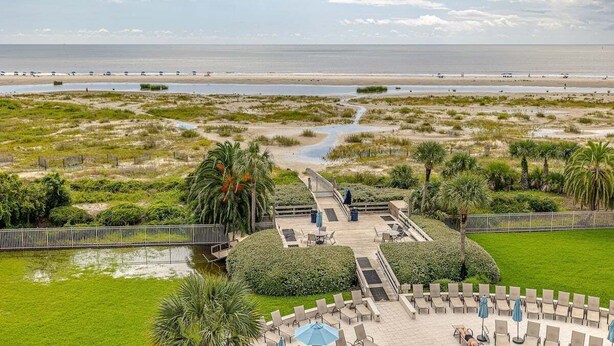 Un resort con zona de piscina, sillones de descanso y vistas a la playa y al océano.