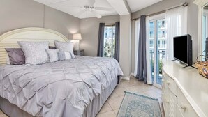 Un dormitorio con cama, ventilador de techo, televisión y ventana con cortinas.
