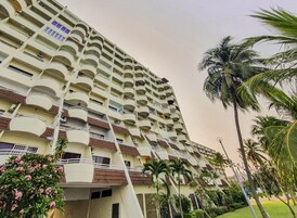 A multi-story hotel with balconies, palm trees, and a garden area.