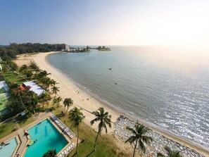 A beach resort with a swimming pool, palm trees, and a view of the ocean. - Seaview Condo Regency  (Port Dickson)