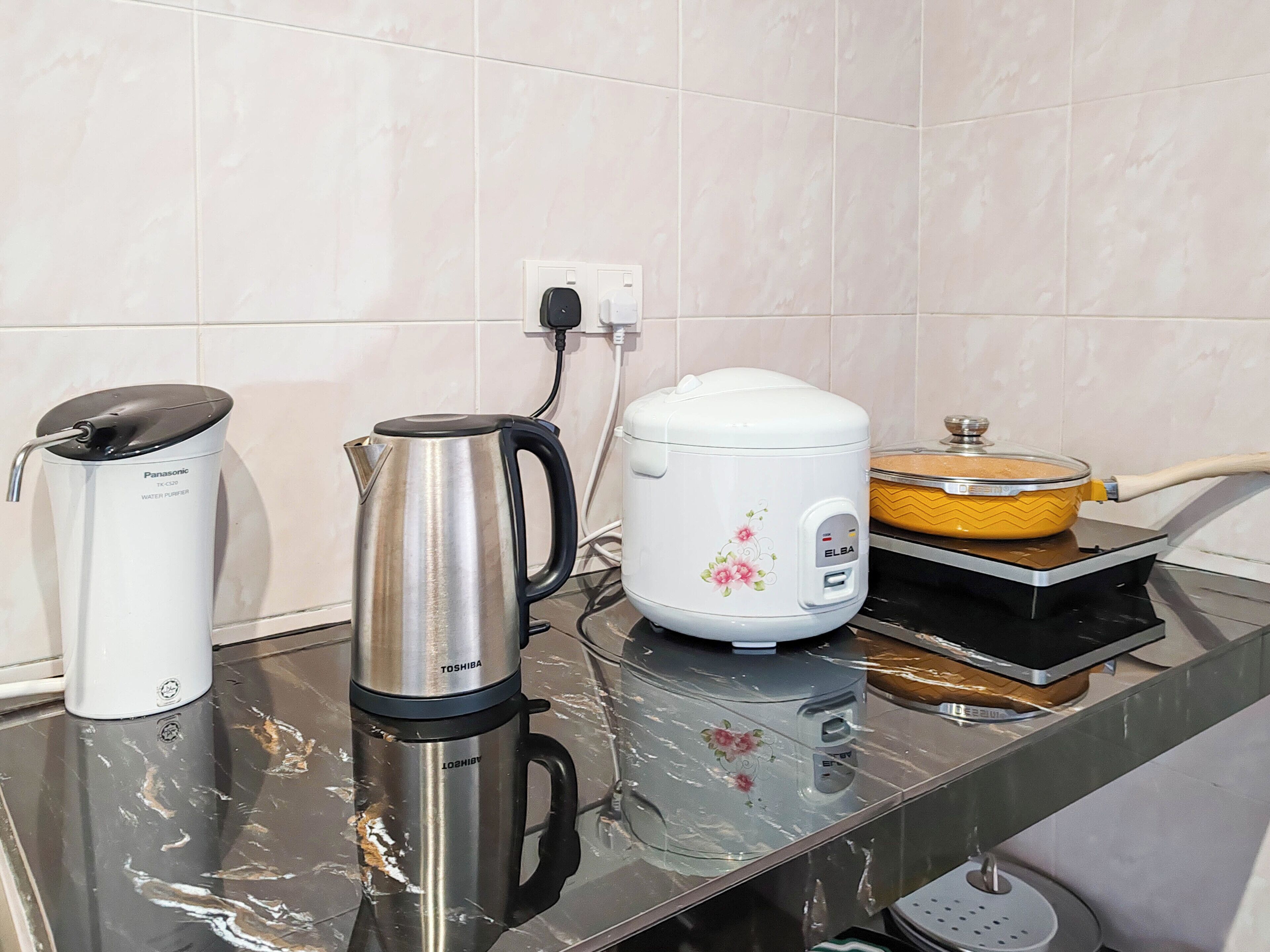A kitchen counter with a water purifier, a stainless steel kettle, a rice cooker, and a yellow pot on an induction stove.
