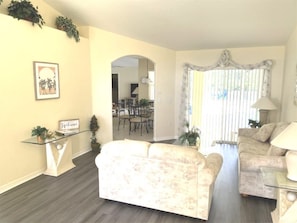 A living room with a beige sofa, a glass coffee table, a lamp, and a dining area in the background. - 4 Bedroom - Budget Home With Private Pool (Davenport)