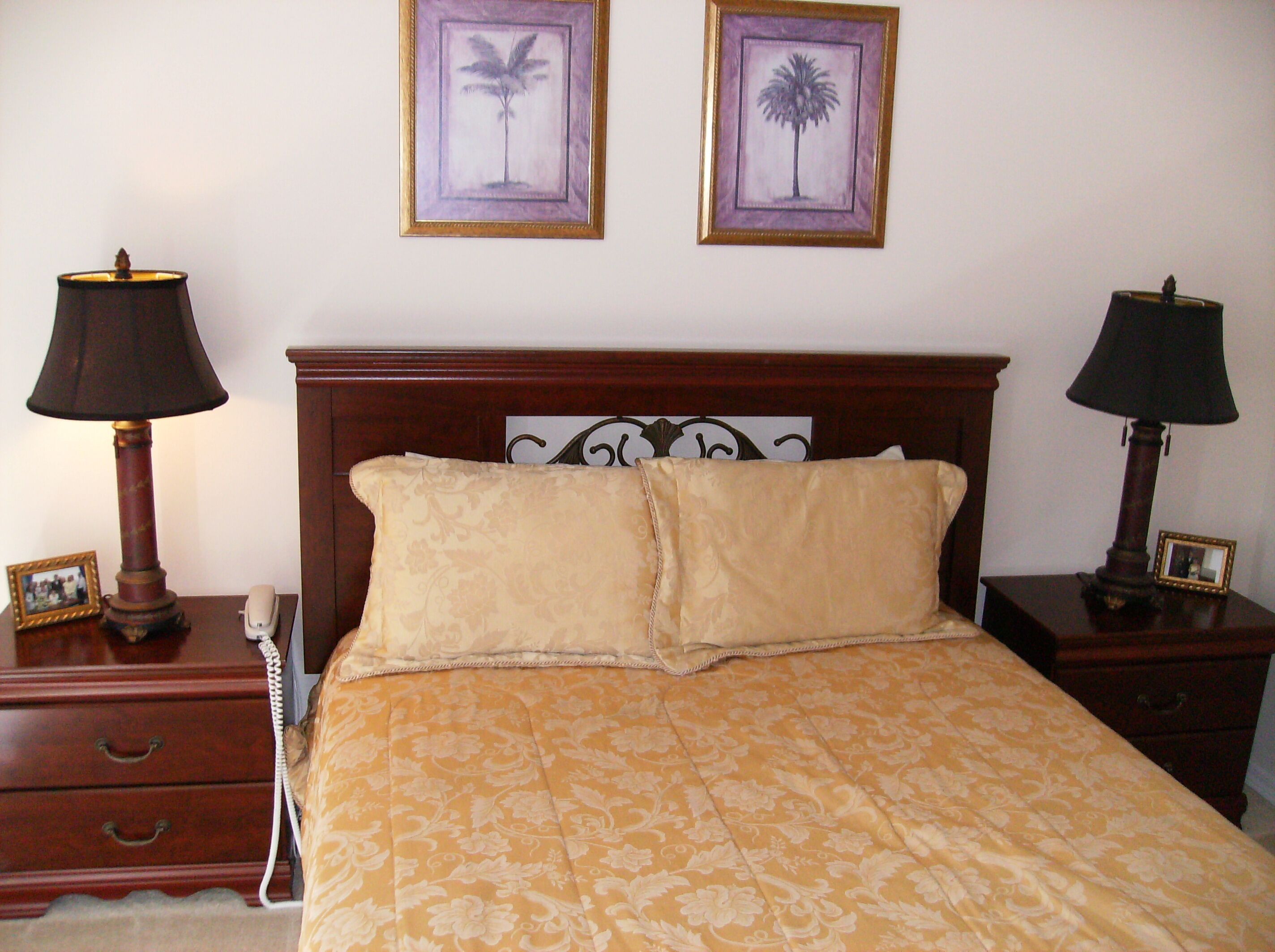 A neatly made bed with a patterned bedspread, two bedside tables with lamps, and two framed pictures on the wall.