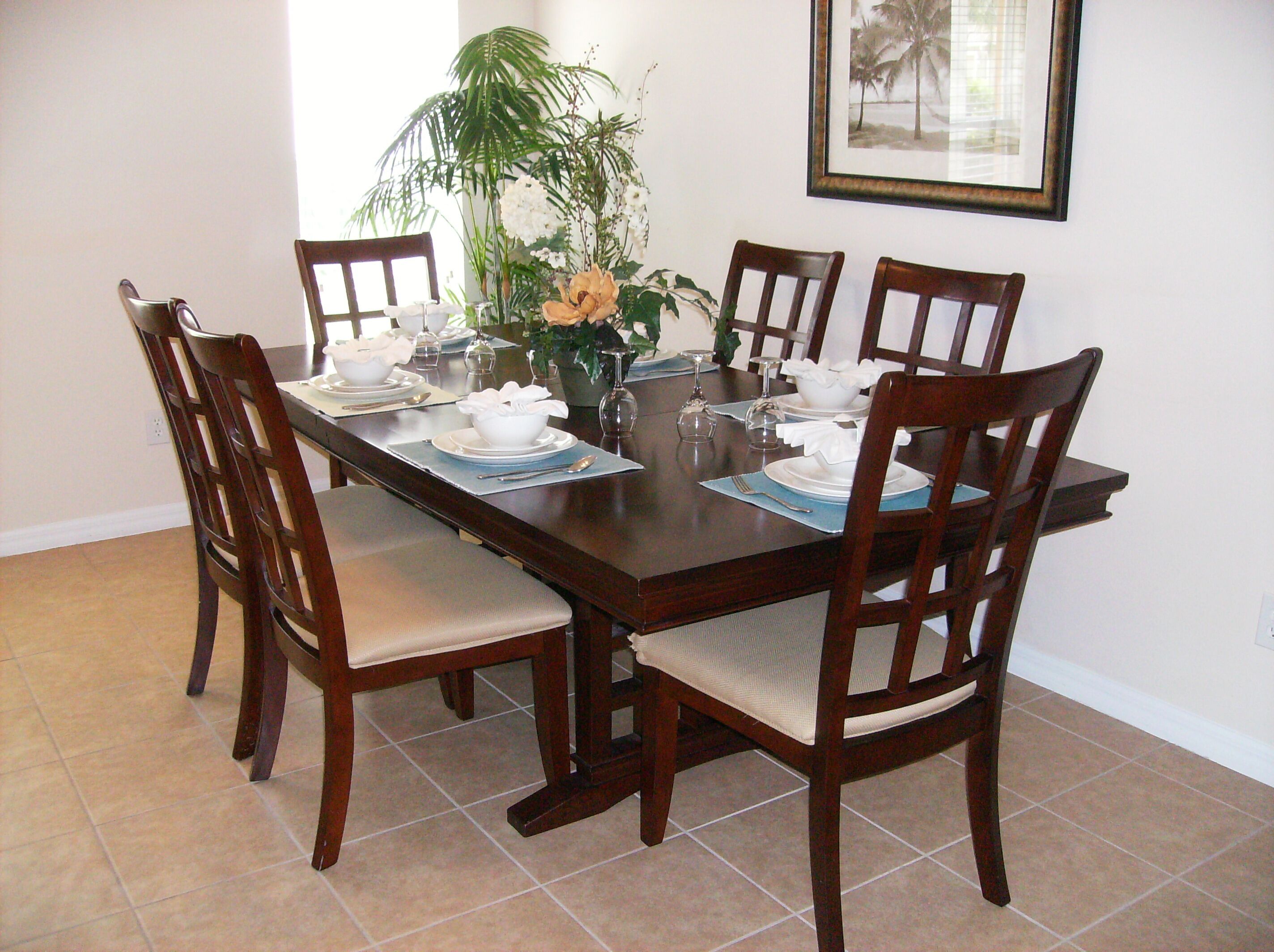 A dining table set for six with chairs, a vase of flowers, and a framed picture on the wall.