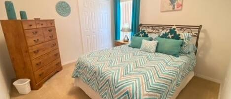 A bedroom with a bed, a dresser, a door, and a wall with a painting.