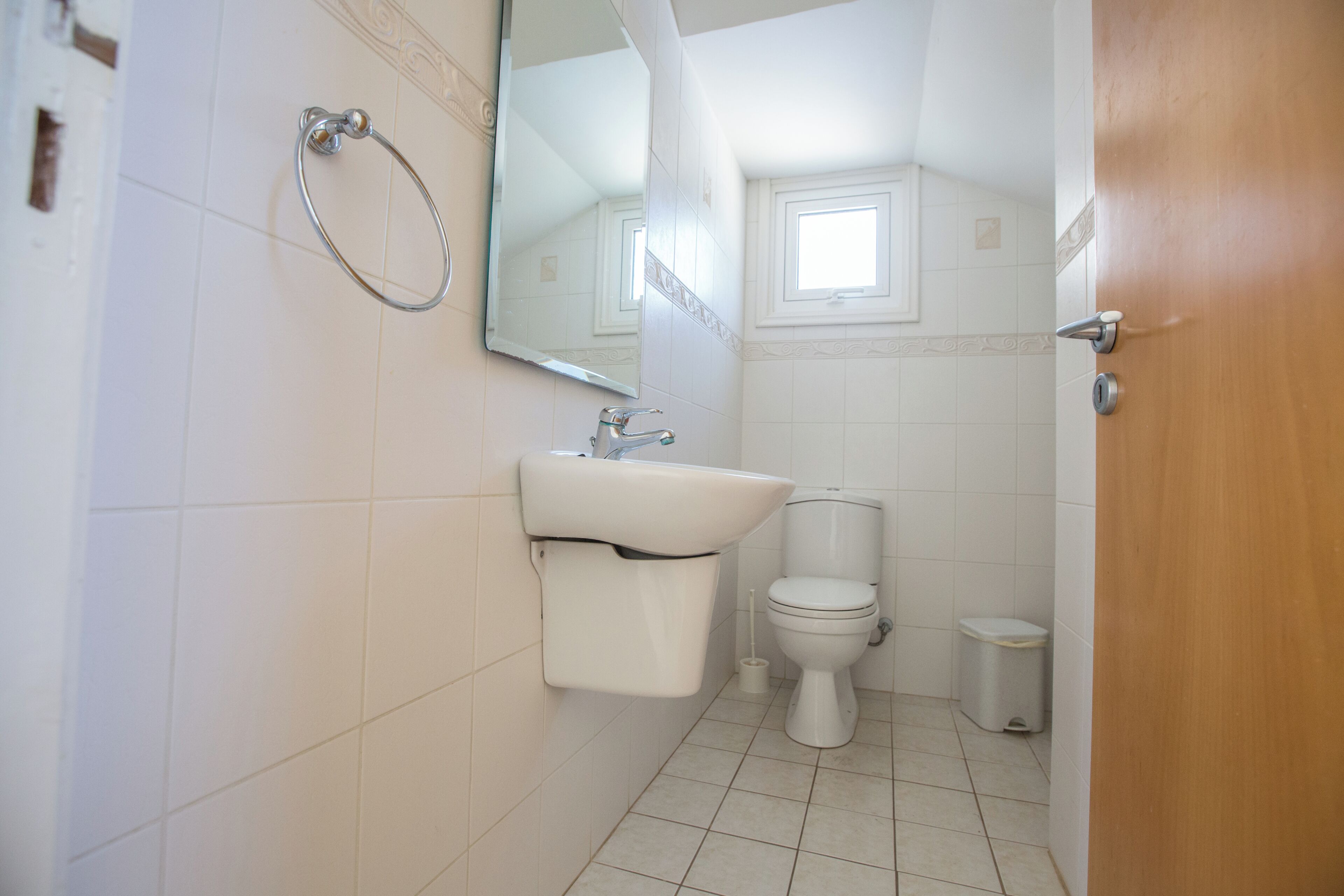 Et lille, rent badeværelse med toilet, vask og spejl.