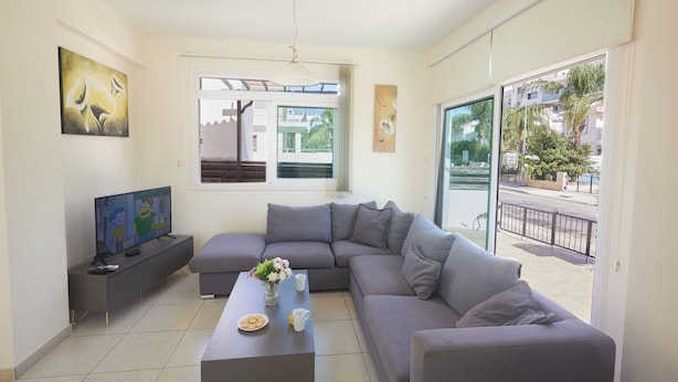 Una sala de estar moderna con un sofá seccional gris, un televisor de pantalla plana, una mesa de centro y una ventana con vista a la calle.