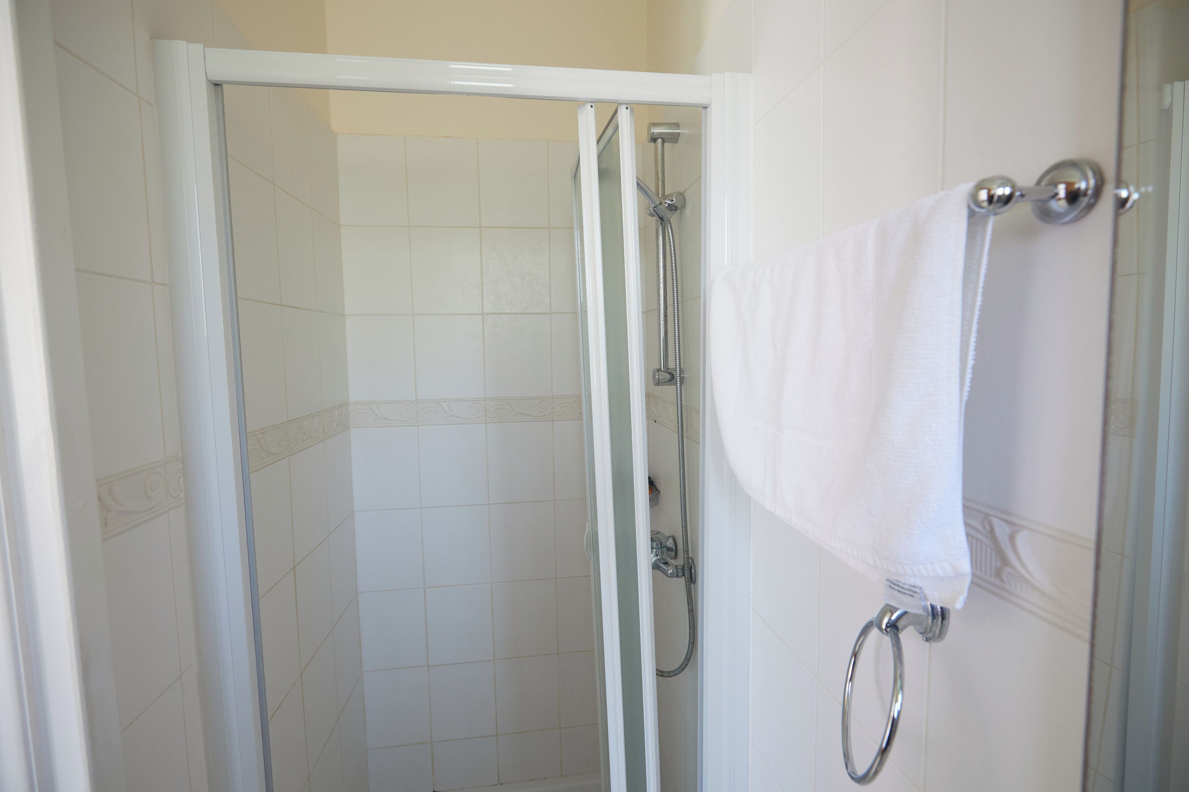 Een douche met een glazen deur, een handdoek aan een metalen ring en betegelde wanden.