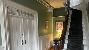 Un pasillo con una puerta blanca, una escalera de madera con alfombra oscura y una pared con un cuadro enmarcado.
