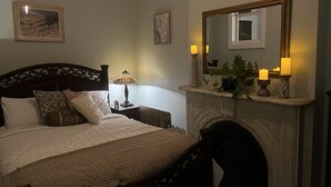 Un dormitorio con cama, mesita de noche, lámpara, espejo y chimenea.