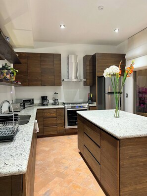 A modern kitchen with wooden cabinets, a stainless steel range, and a central island with a vase of flowers. - Malen House San Miguel de Allende Mexico (San Miguel de Allende)