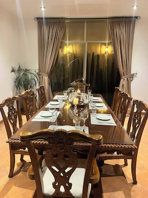 A dining table set for six with wooden chairs, a candle centerpiece, and a view through a window with curtains. - Malen House San Miguel de Allende Mexico (San Miguel de Allende)