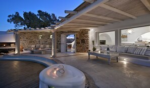 Uma área de estar ao ar livre moderna com paredes de pedra, pérgola de madeira e piscina.