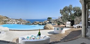 A pool area with a clear view of the sea and a stone structure with a plant on top.