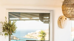 A cozy seating area with a view of the sea, a table set with glasses, and a hanging light fixture. - Paraga Scorpios Villa1 hot tub 7 Mins Walk to Beach by Calypso Sunset Villas (Mykonos)