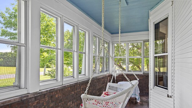 A room with large windows, a brick wall, and a white wicker swing chair.