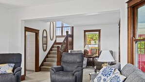 A spacious living room with a grey sofa, a leather armchair, and a wooden staircase leading to an upper floor.
