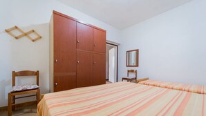 A bedroom with a bed, a wooden wardrobe, a chair, and a mirror on the wall. - APPARTAMENTI CAMPO AL PERO - CAMPO AL PERO - TRILO 3 (Rio dell'Elba)
