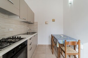 A compact kitchen with a gas stove, oven, and sink, a dining table with chairs, and a small wall-mounted light fixture.