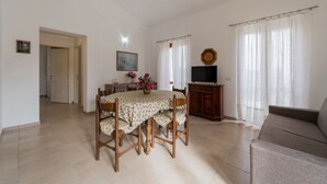 Una sala de estar con una mesa de comedor, sillas, un sofá, un televisor y un cuadro en la pared.