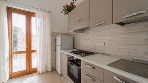 Una cocina moderna con estufa a gas, horno y refrigerador. Hay una puerta corrediza de vidrio con vistas al exterior.