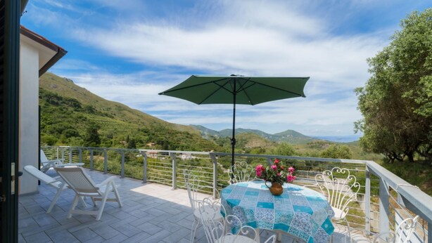 Una terraza con mesa y sillas, un paraguas verde y vistas a colinas verdes.