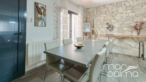 Un espace repas moderne avec un mur en pierre, une grande table et des chaises blanches.