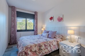 Una camera da letto con un letto, un comodino, una finestra con tende e opere d'arte alle pareti.
