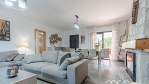 Un salon moderne avec un canapé gris, une table basse et une cheminée. On aperçoit à l’arrière-plan un coin repas avec une table et des chaises.