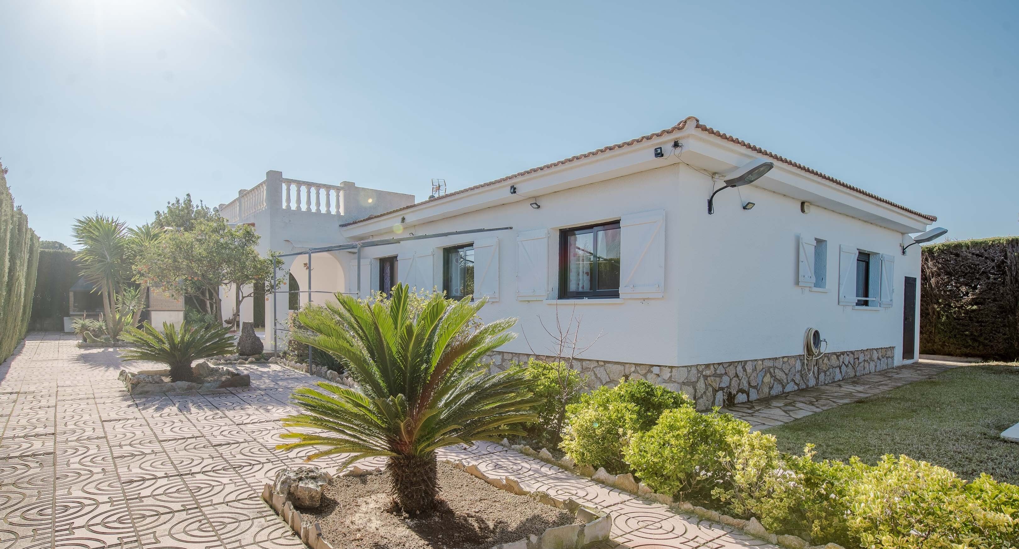 A white building with a tiled patio, palm trees, and a stone wall.