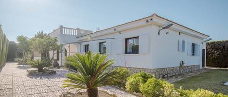 A white building with a tiled patio, palm trees, and a stone wall.