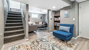 Un salon moderne avec un escalier, un canapé bleu, une bibliothèque et un tapis à motifs.
