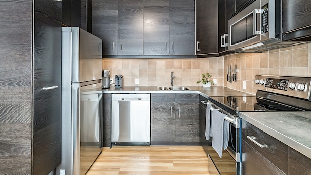 Une cuisine moderne avec des meubles en bois foncé, des appareils électroménagers en acier inoxydable et un dosseret carrelé.