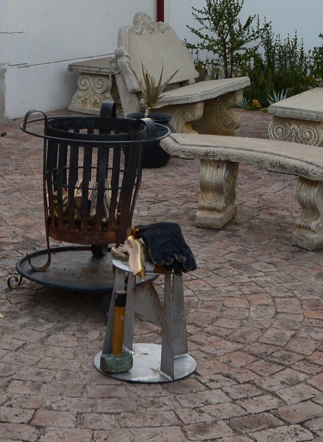 Un patio con un brasero de metal, un banco de piedra y una maceta de piedra decorativa.