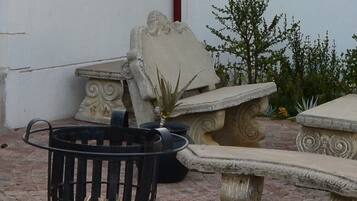 Un patio con un brasero de metal, un banco de piedra y una maceta de piedra decorativa.