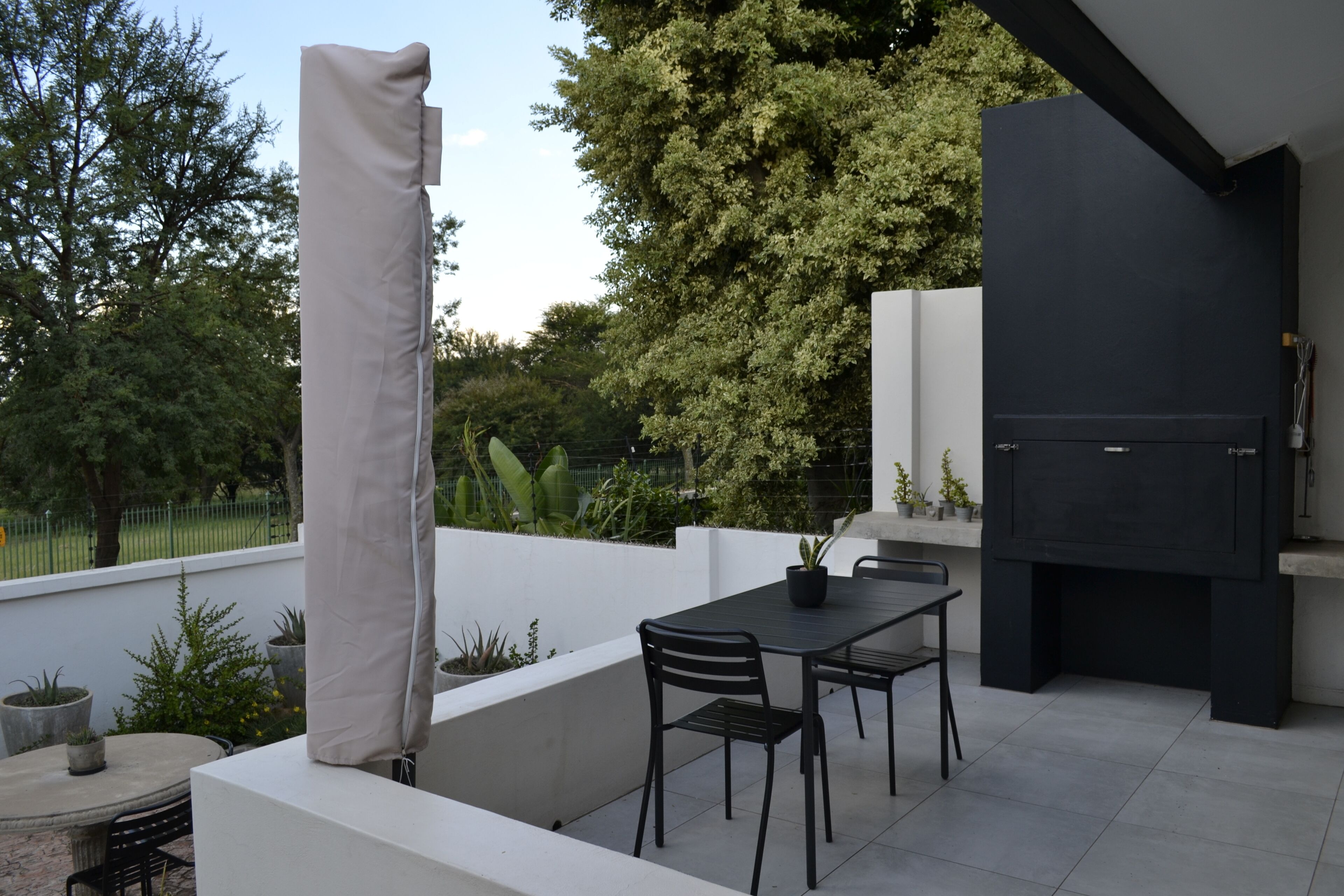 Eine Terrassenanlage im Freien mit Tisch, Stühlen, einem Grill und Kübelpflanzen.