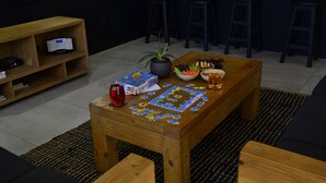 Ein Holztisch mit einem Puzzle, einer Topfpflanze, einer Snackschale und einem Getränkglas.