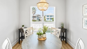 A dining area with a round table, two chairs, a chandelier, and potted plants.