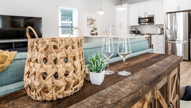 A kitchen with a wooden table, a woven basket, a potted plant, and two wine glasses.